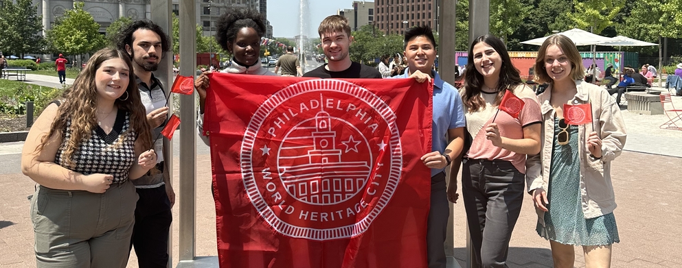 Global Philadelphia interns holding small red flags and a large red flag in the center, all with the Philadelphia World Heritage City Seal standing in front of the LOVE statue.